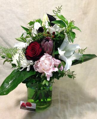 Ανθοπωλείο . Μπουκέτο με άνθη εποχής σε  γυάλινο βάζο με στρώσεις χρωματιστής διακοσμητικής άμμου